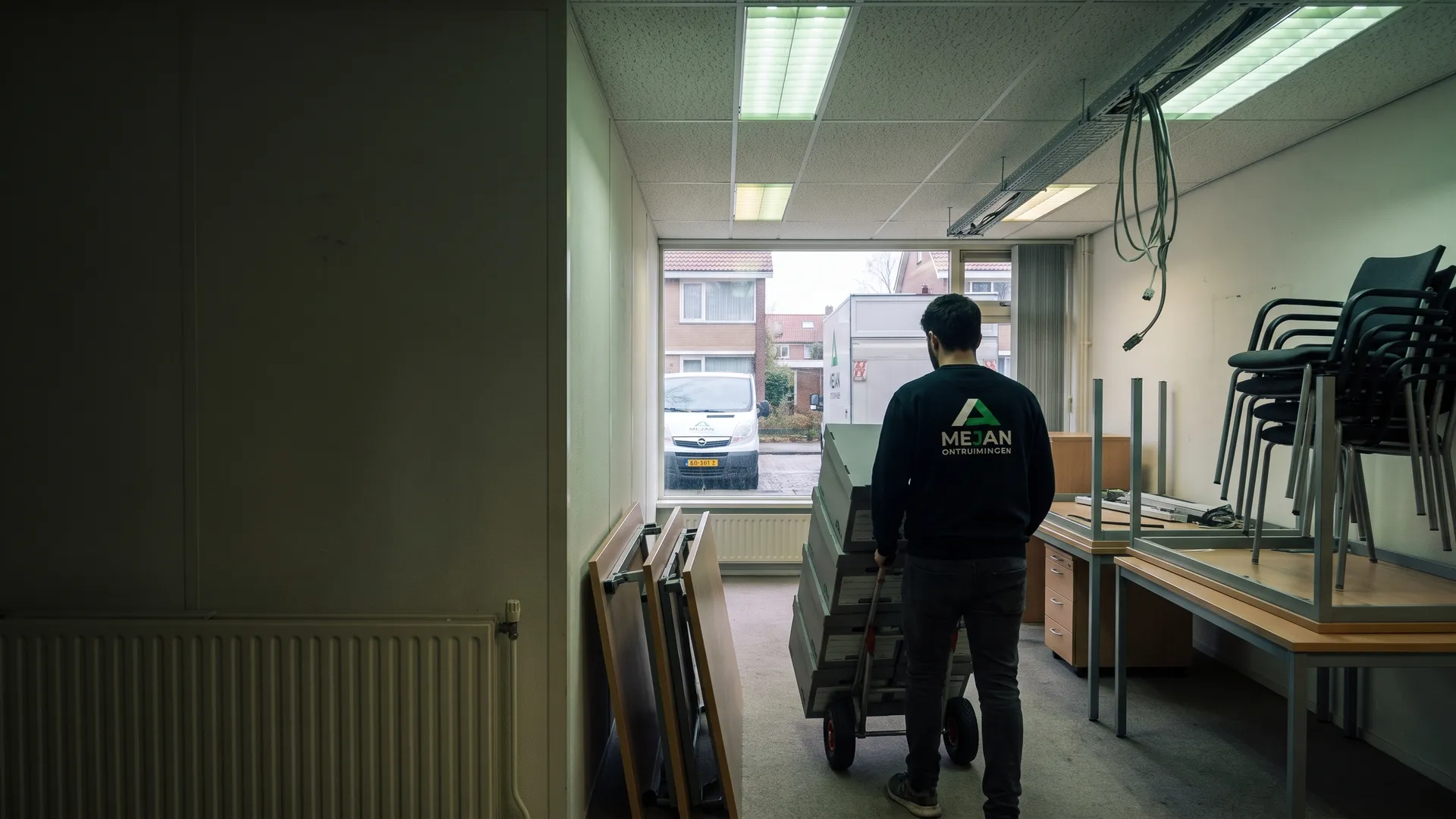 Medewerker rijdt archiefdozen op een steekwagen door het leeggehaalde kantoor