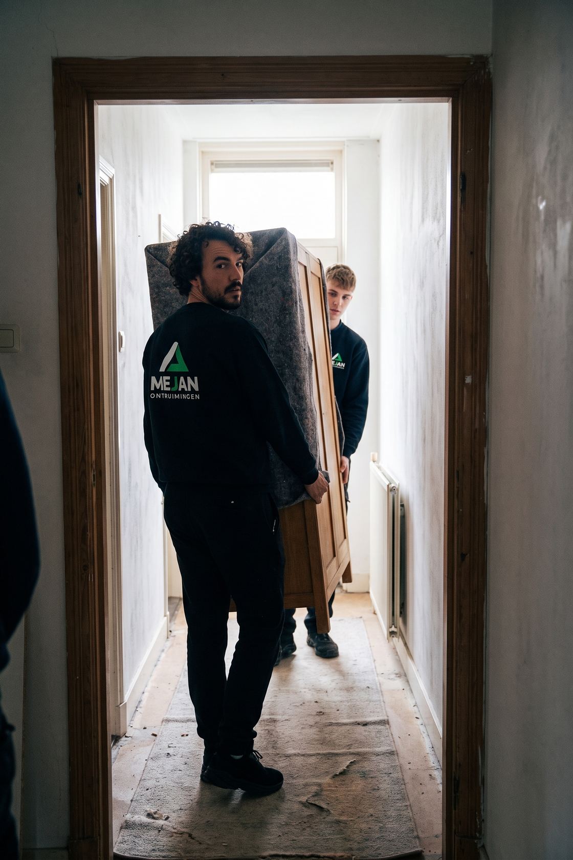 Twee medewerkers dragen een kast in dekens door de gang