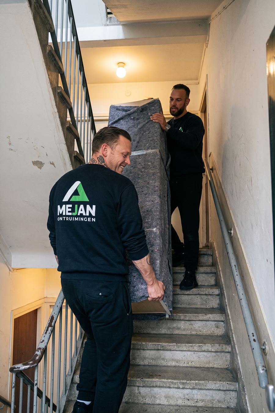 Medewerkers dragen ingepakte spullen in dekens het trappenhuis door
